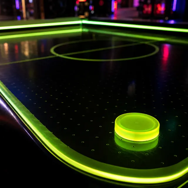 Detalle de una mesa de aeroahockey con disco luminoso en verde lima